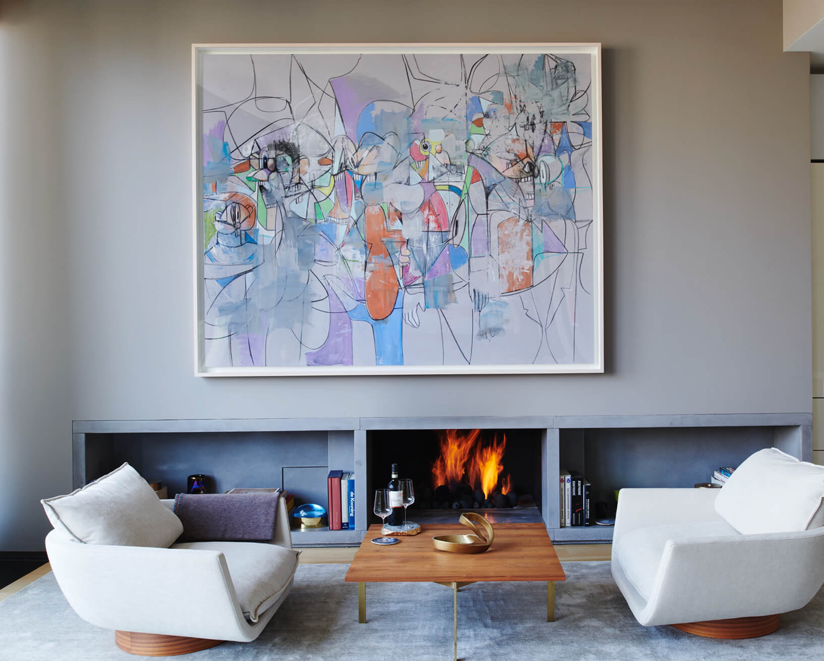 CNR Group NYC luxury home project management: Modern living room with two white cushioned chairs, a wooden coffee table, and a fireplace beneath a large abstract painting.