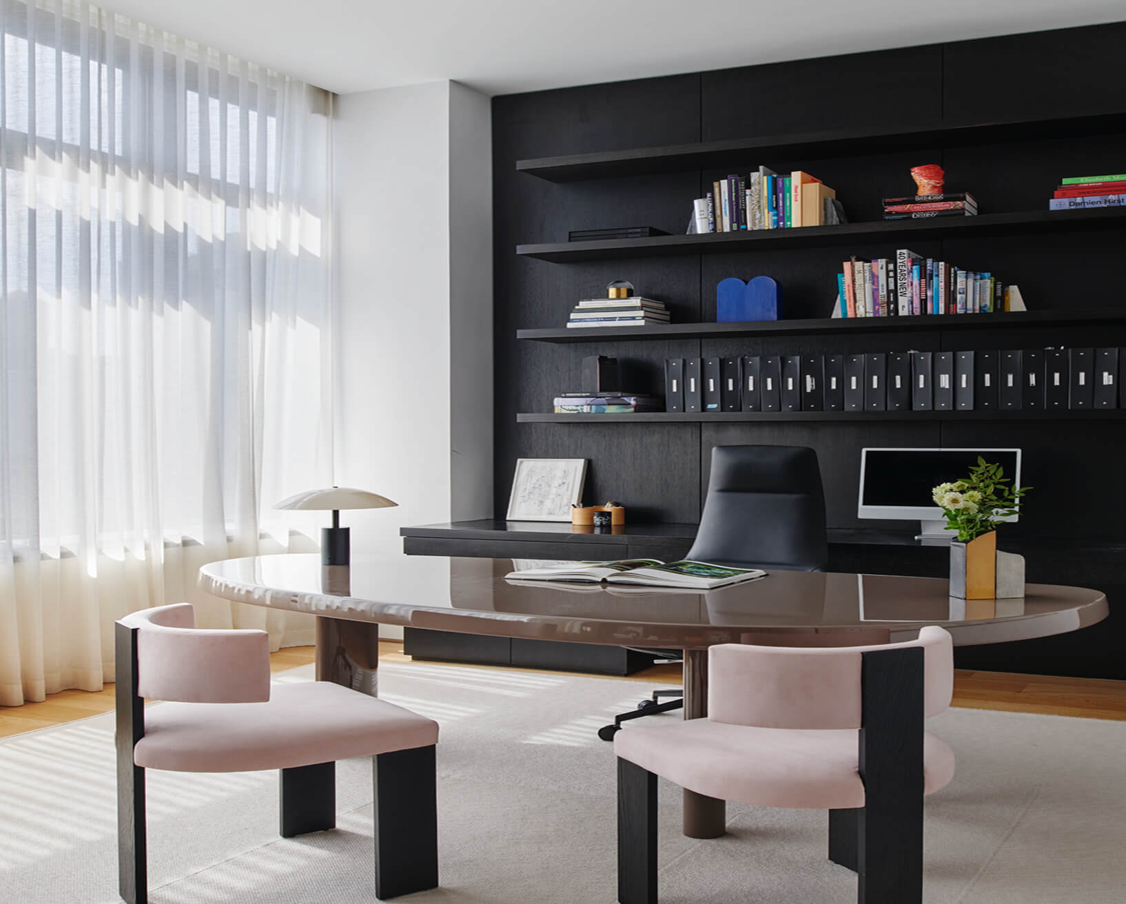 CNR Group NYC luxury home project management: Modern office with oval glossy table, black swivel chair, pink cushioned chairs, and black shelves filled with books and files.