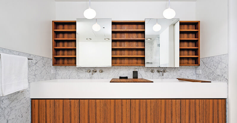 Modern bathroom vanity with white countertop, custom millwork wooden cabinets, two mirrors, open wooden shelves, and marble backsplash.