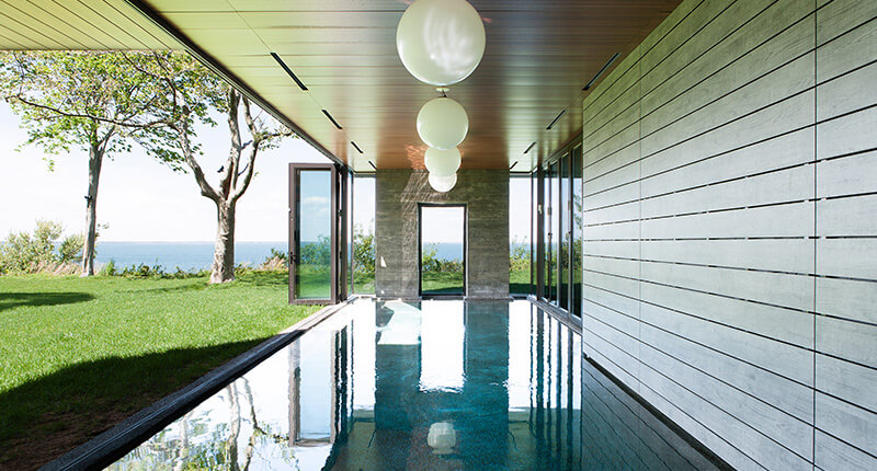 CNR Group luxury home construction interior: Modern indoor swimming pool with large glass doors open to a green lawn and ocean view.