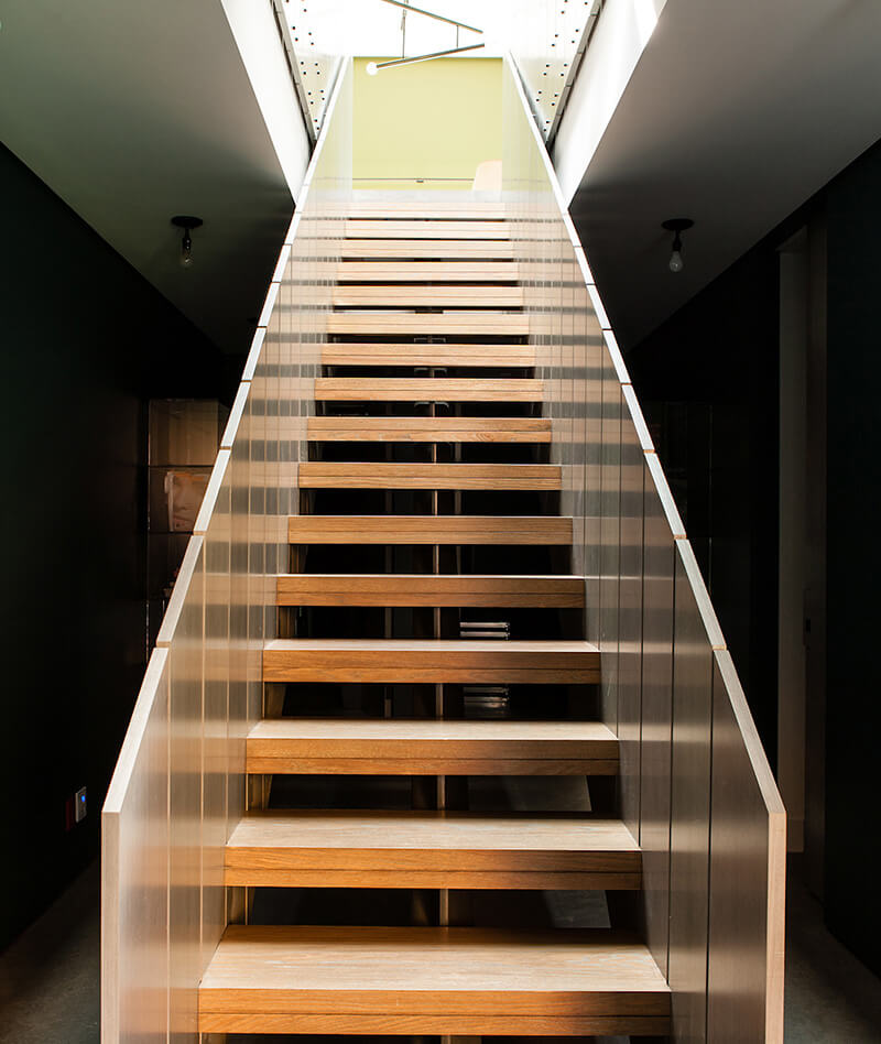 Modern custom millwork wooden staircase with clear glass railings leading up to a bright, sunlit room.