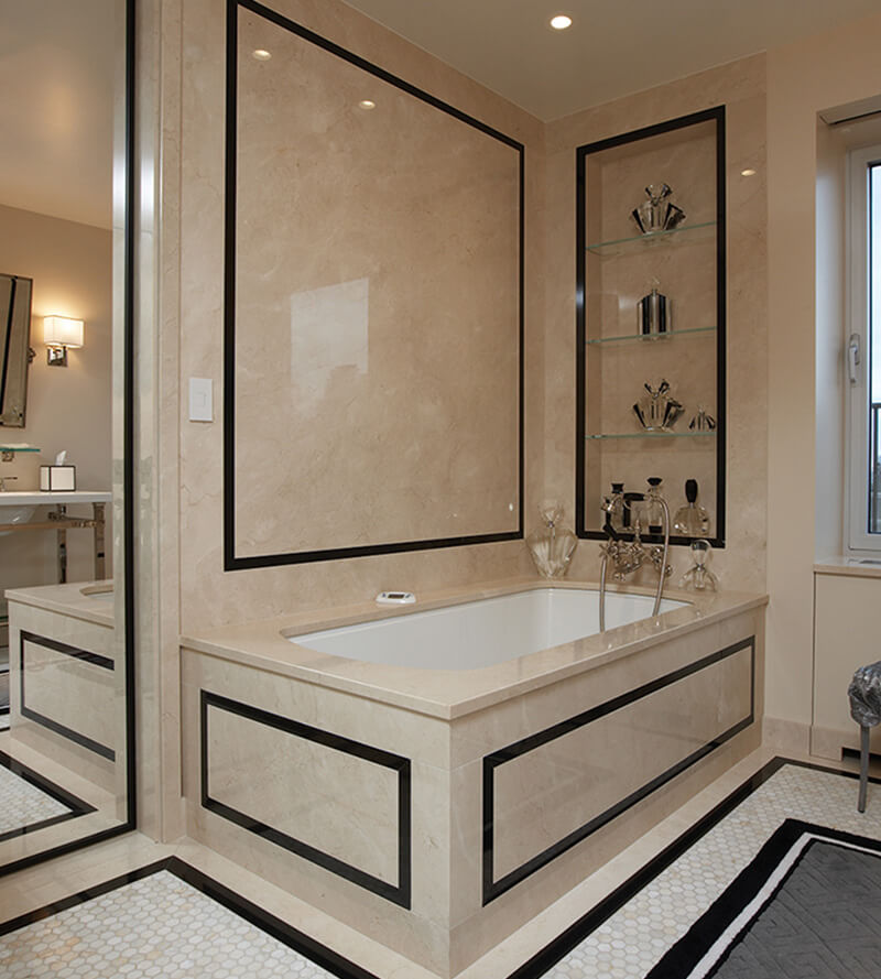 CNR Group luxury home construction interior: Elegant beige marble bathroom with a built-in bathtub featuring black trim, glass shelves with decorative items, and a large window.