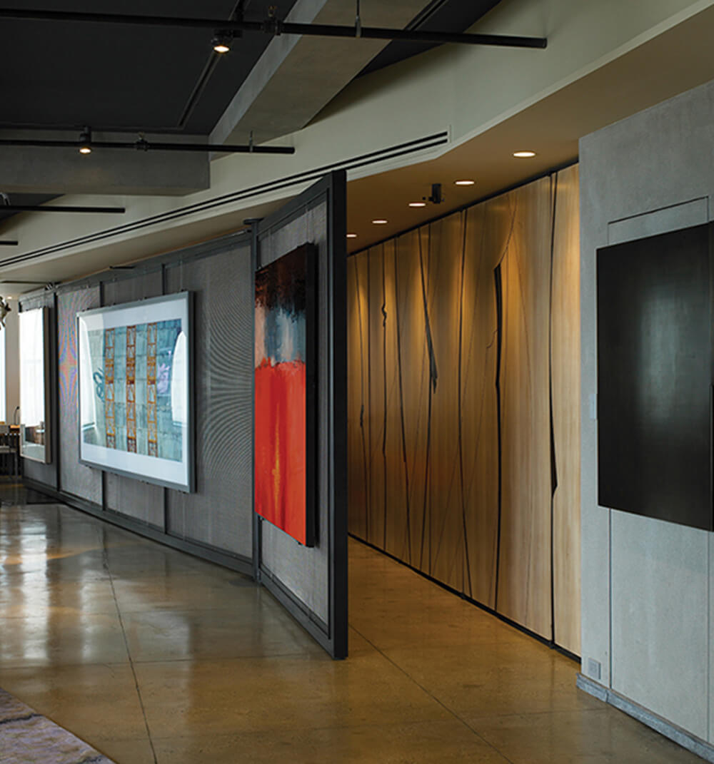 CNR Group luxury home construction interior: Modern hallway with polished concrete floor, backlit wooden wall panels, and abstract art pieces displayed on walls and partitions.