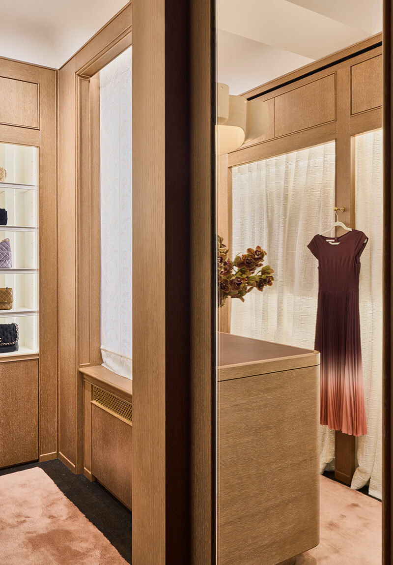 Luxurious walk-in closet with custom millwork wood paneling, a display cabinet with handbags, a full-length mirror, and an ombré dress hanging on a hook.