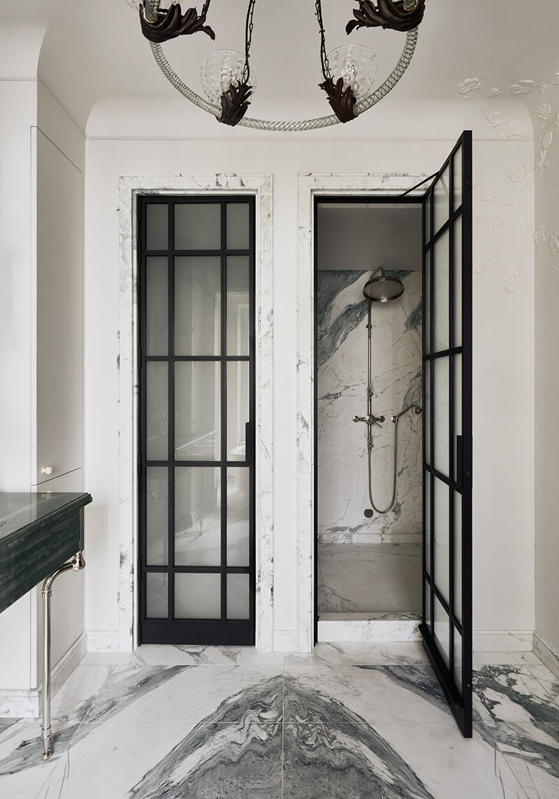 CNR Group luxury home construction interior: Modern bathroom with black-framed glass shower door open to a marble shower interior, next to a closed matching door and a green marble countertop.
