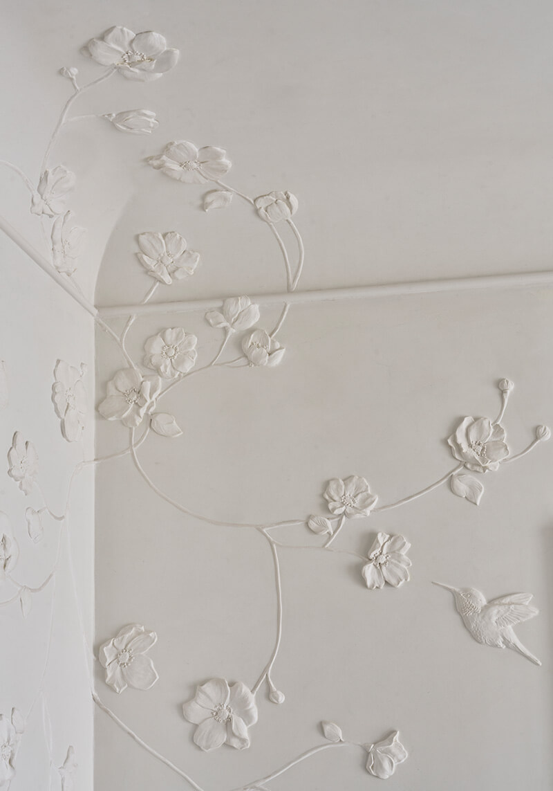 Custom millwork white embossed floral and hummingbird design decorating a corner wall and ceiling.