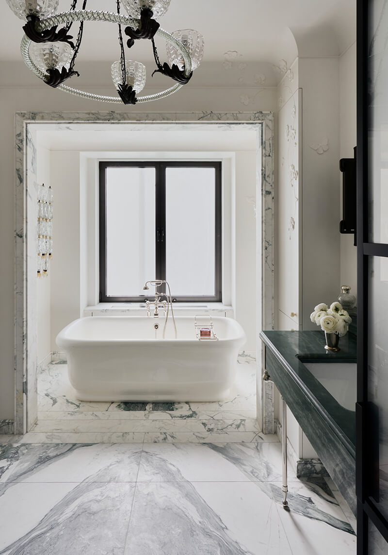 CNR Group NYC luxury home project management interior: Modern bathroom with a white freestanding bathtub on marble flooring and a dark green countertop with a vase of white roses.