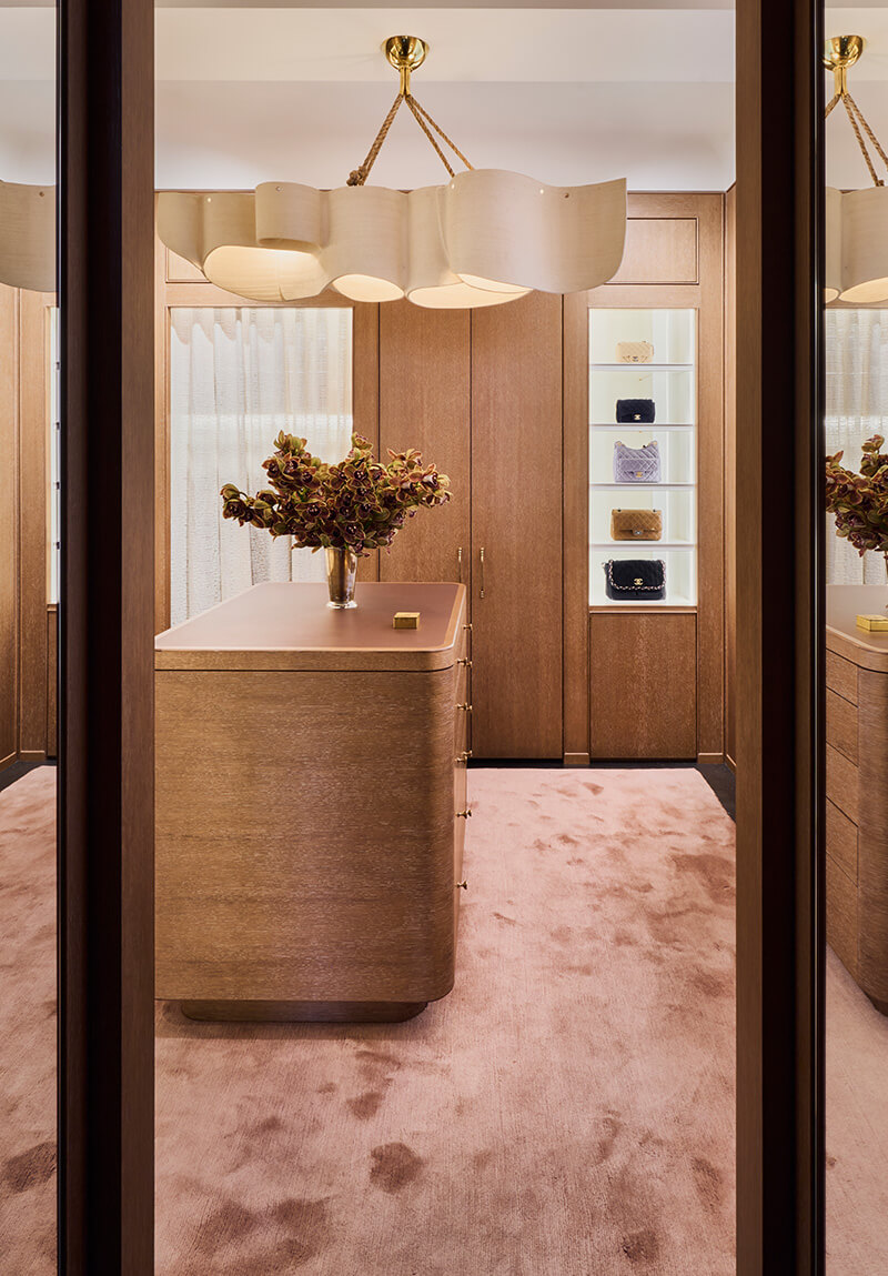 CNR Group luxury home construction interior: Elegant walk-in closet with wooden island, pink carpet, modern chandelier, and shelves displaying designer handbags.