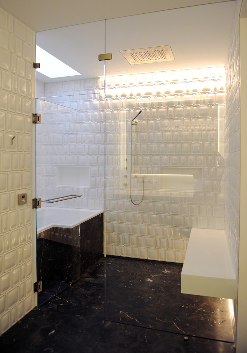 CNR Group luxury home project management interior: Modern bathroom with white textured wall tiles, black marble floor, glass shower enclosure, and built-in bathtub.