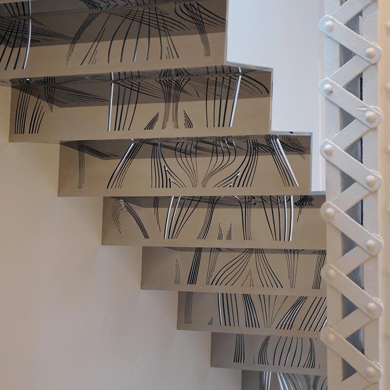 Close-up of a modern custom metalworks staircase with reflective steps featuring black abstract line patterns and a white riveted metal support beam.