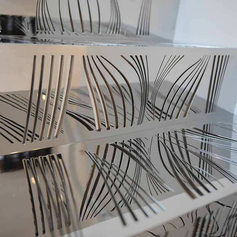 Close-up of metalwork stairs with decorative cut-out wavy line patterns reflecting light.