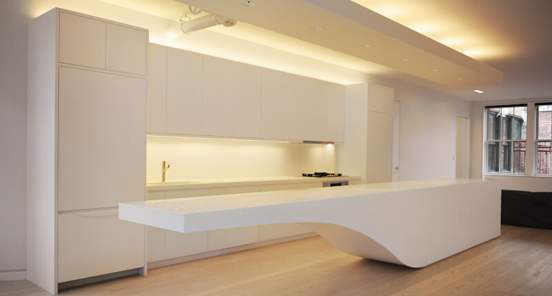 CNR Group luxury home construction interior: Modern minimalist kitchen with a long white island featuring a curved underside and sleek white custom millwork cabinetry.