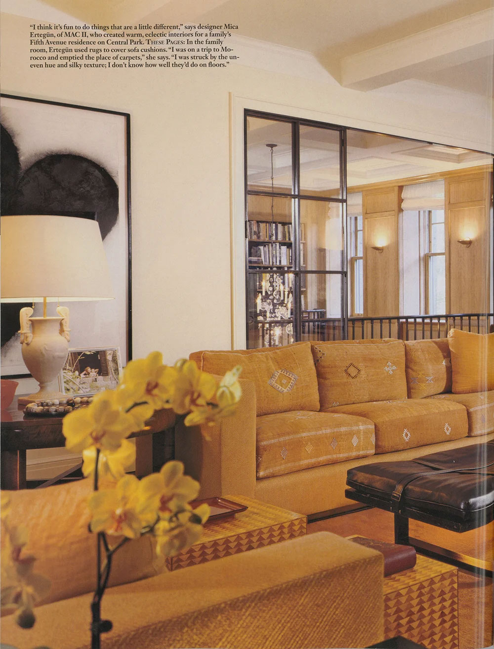 Magazine page featuring CNR Group luxury home builders project interior: Warm, eclectic living room with mustard yellow sofas, a floral centerpiece, a large black and white abstract painting, and a lamp on a side table, with a view into a bright room through glass panels.