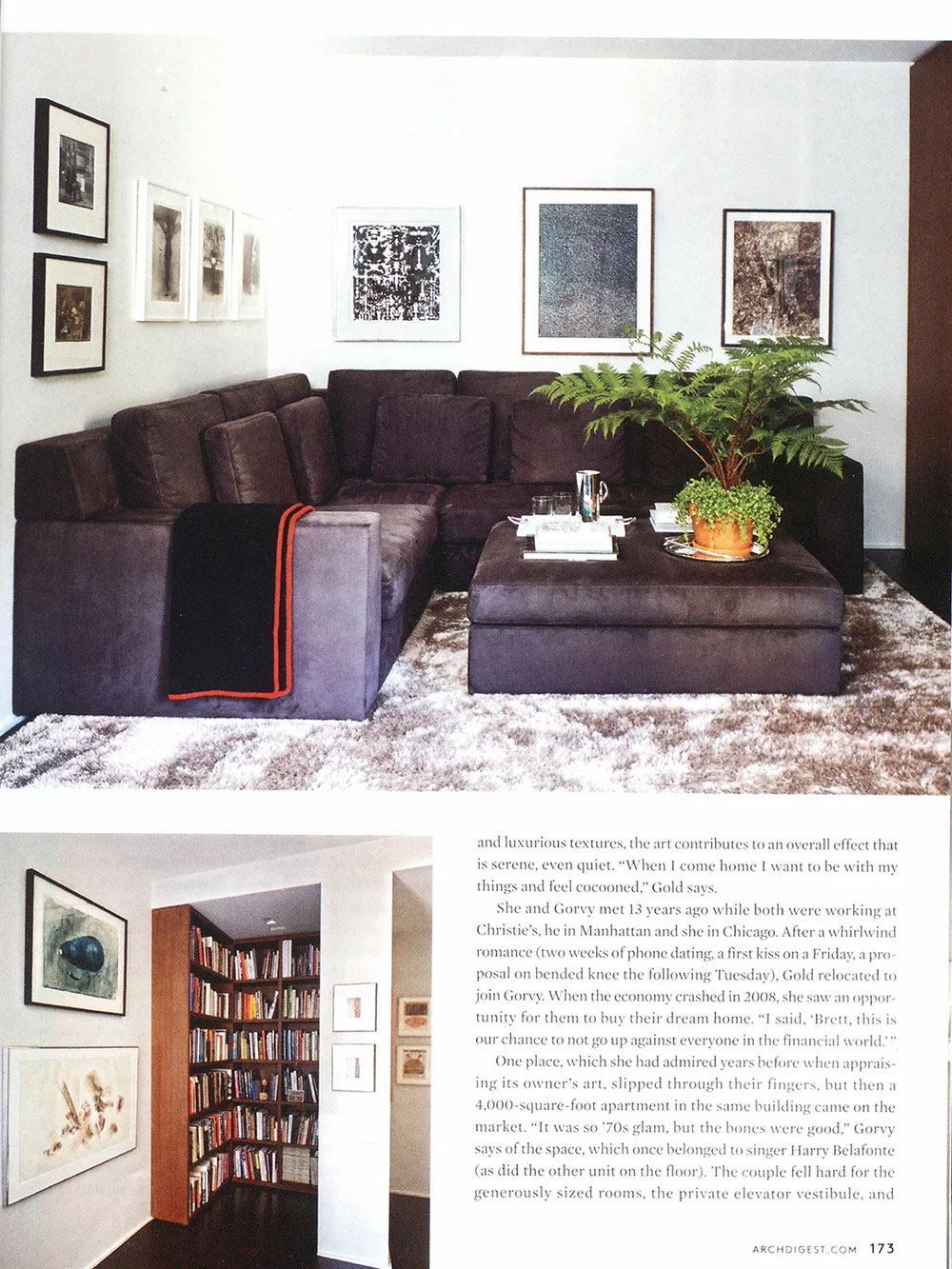 CNR Group luxury home interior: Modern living room with a dark grey sectional sofa, a large ottoman with a potted plant, black blanket with red trim, abstract framed art on white walls, and a plush light carpet.