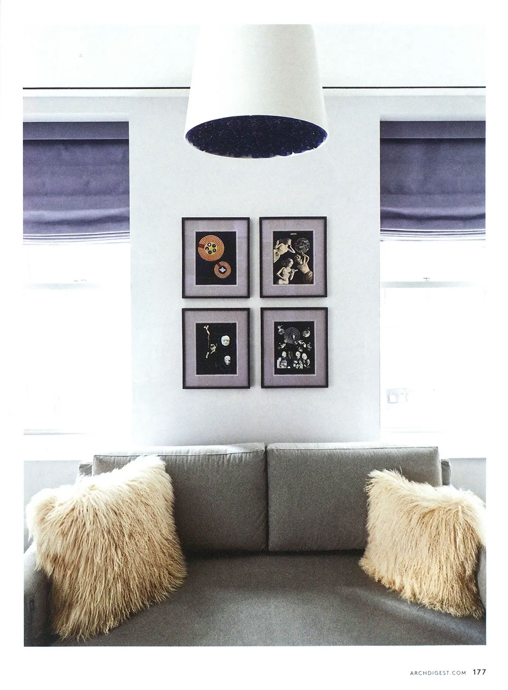 CNR Group luxury home interior: a minimalist living room with a gray sofa, two beige fluffy pillows, four framed abstract artworks on the white wall, and blue Roman shades on the windows.