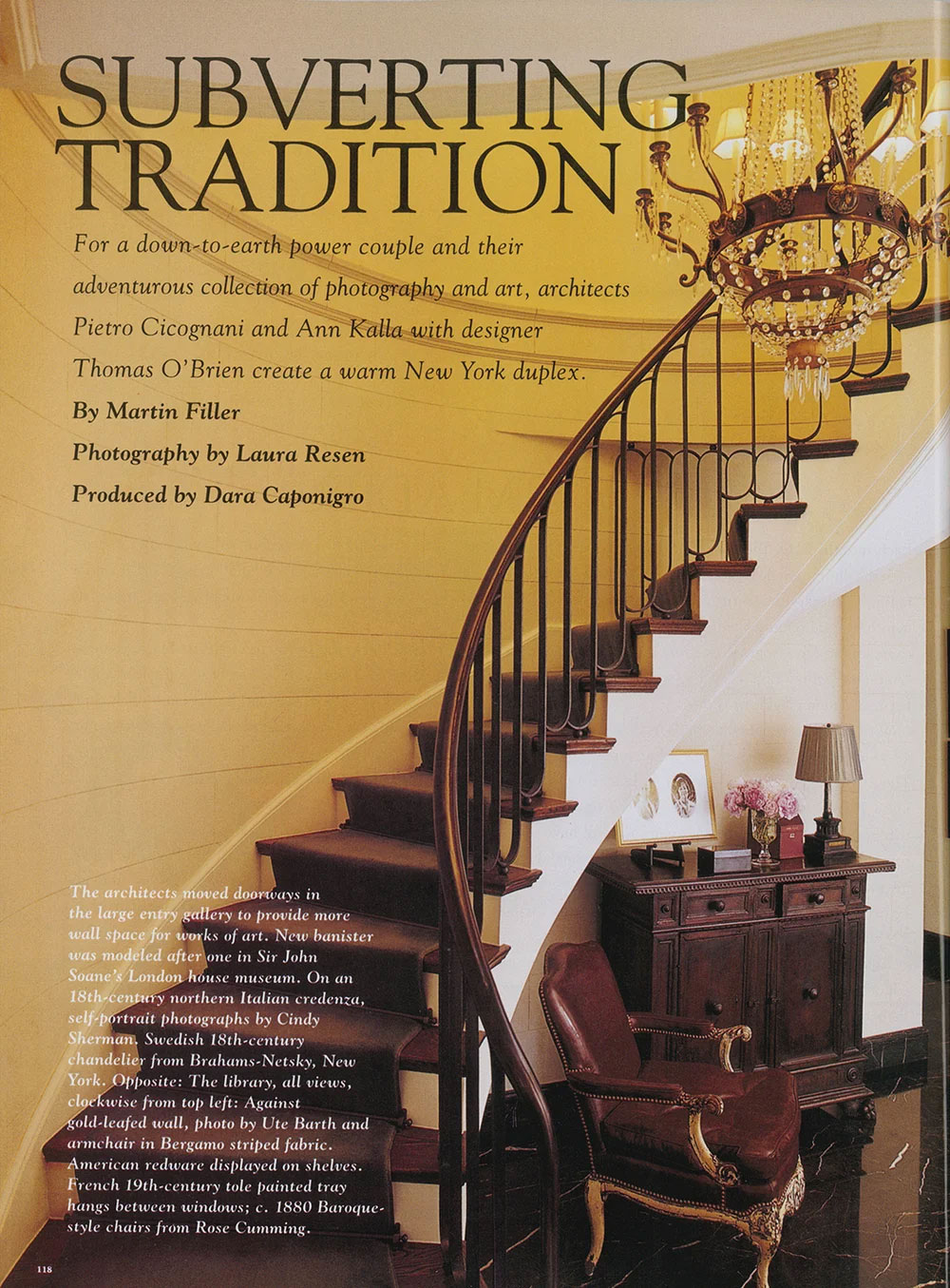 Curved staircase with dark wooden steps and black iron railing, showcasing CNR Group's custom millwork and metalwork, next to a vintage armchair and wooden cabinet under the stairs, with a chandelier overhead.