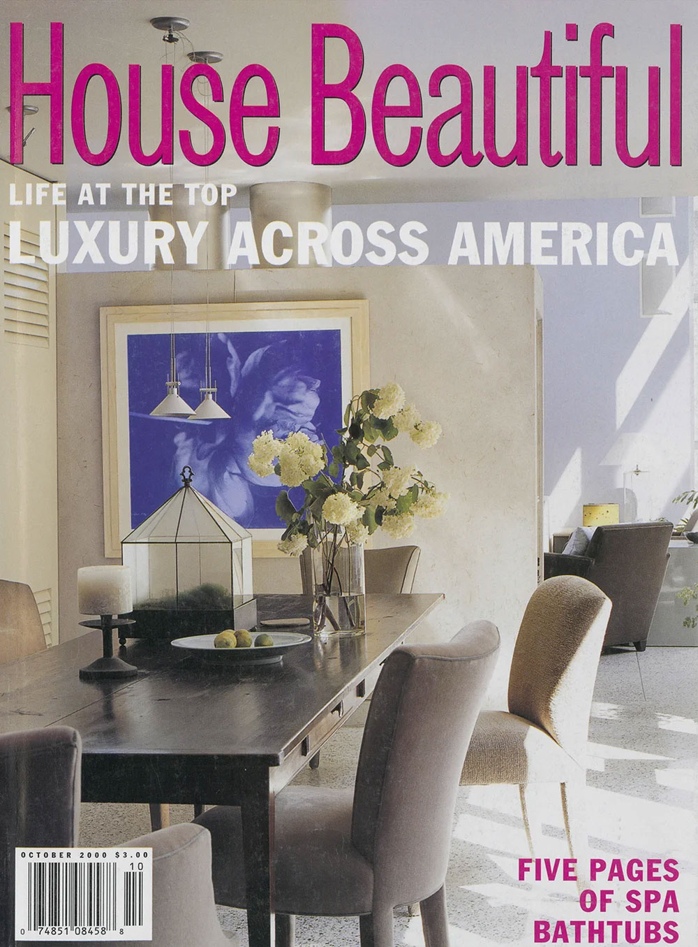 The cover of a House Beautiful magazine issue that features CNR Group luxury home builders. The cover shows a modern dining room with a dark wooden table, six upholstered chairs, a glass vase with white flowers, a framed blue artwork, and sunlight streaming through windows.