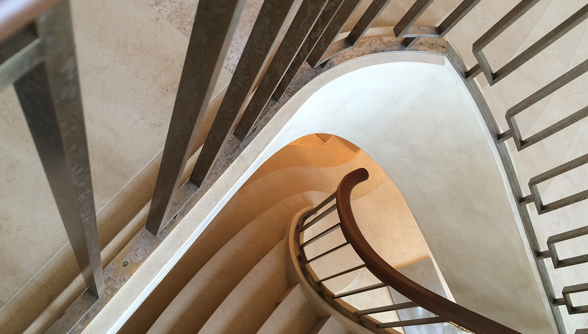 Top-down view of a curved staircase with CNR Group custom metalwork railings and beige steps.