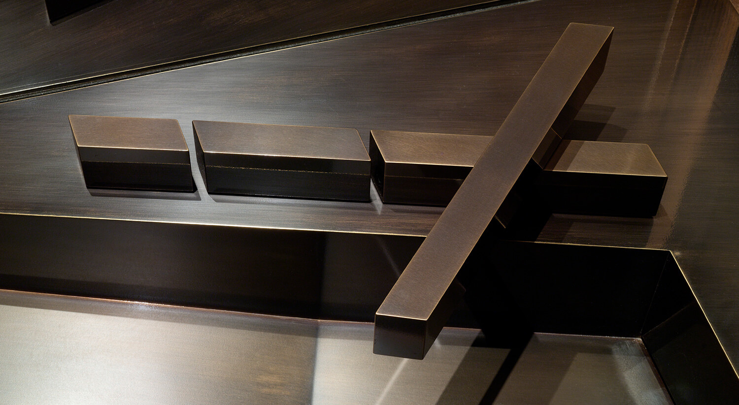 Close-up of CNR Group custom metalworking: modern brushed metal faucet handles and spout with a dark bronze finish.