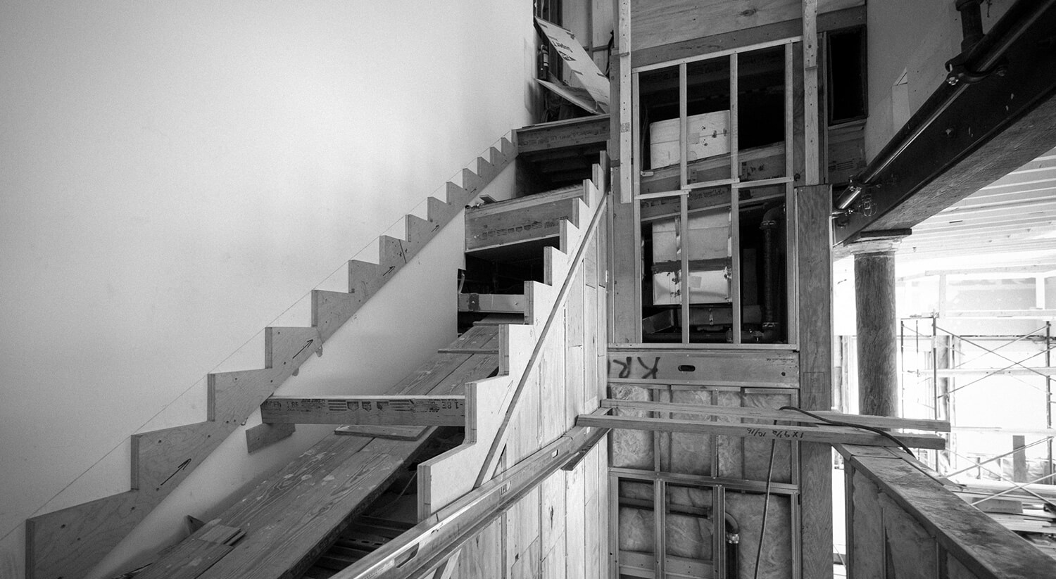 Black and white photo of CNR Group custom millwork showcasing an indoor wooden staircase under construction with exposed framing and insulation.