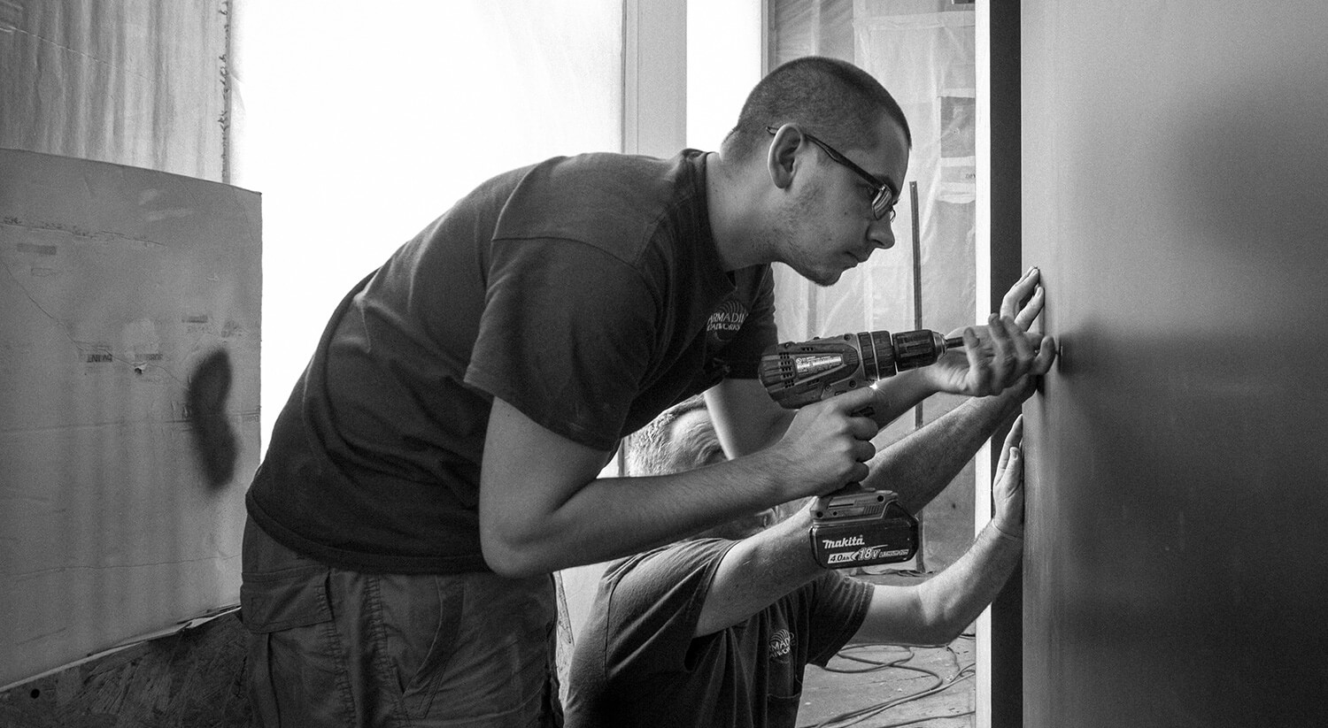 Two men working together on CNR Group NYC luxury home project management as they drill into a wall, one holding the cordless drill and the other steadying the surface.