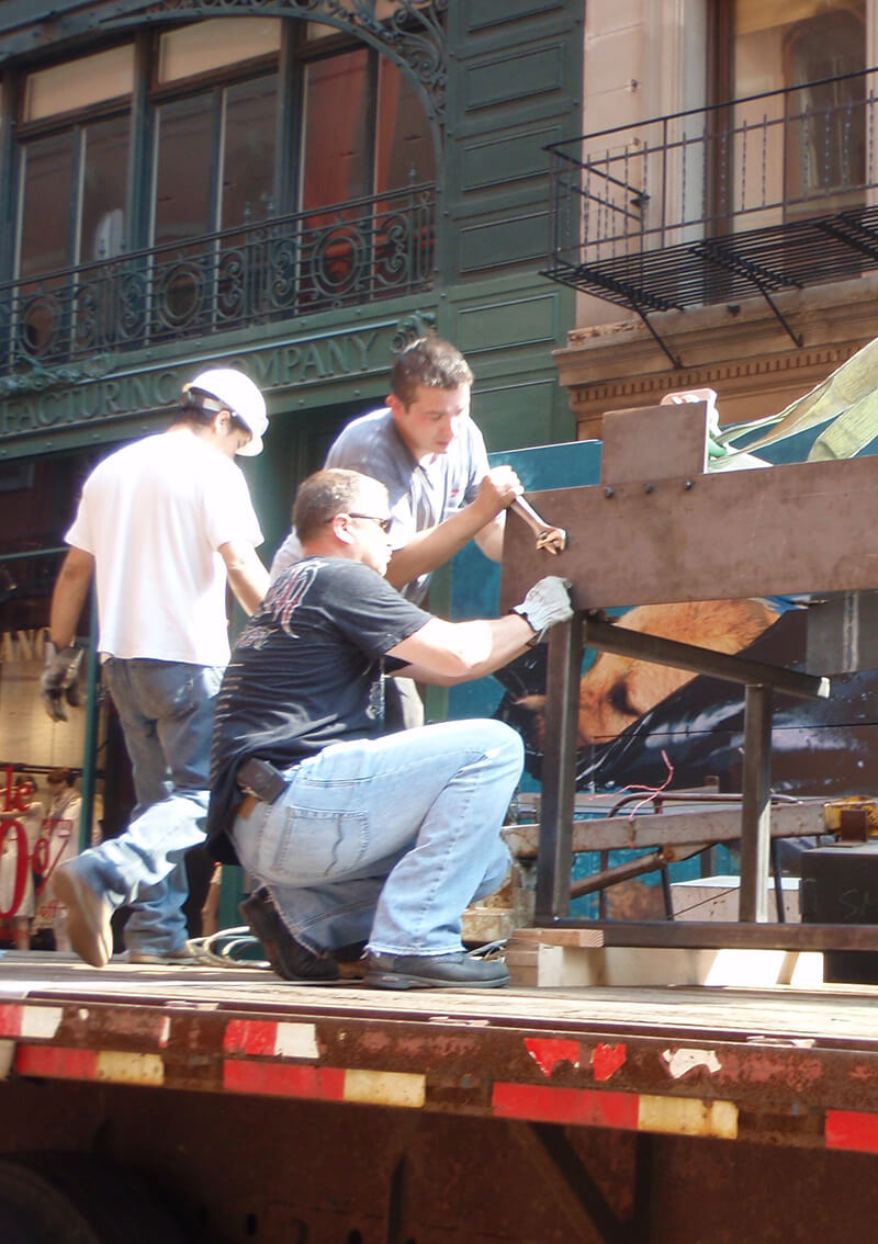 Three CNR Group NYC luxury home construction workers assembling a metal structure on a flatbed truck in an urban setting.