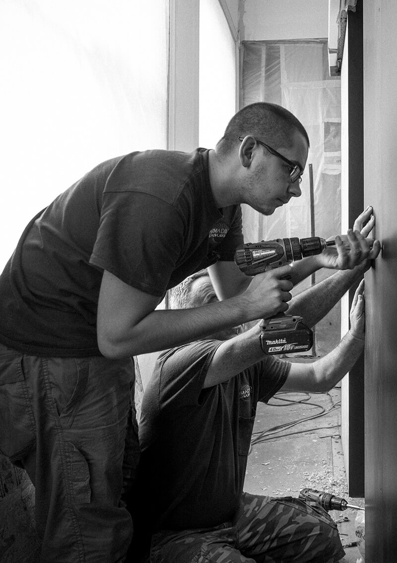 Two men working on luxury home project management for CNR Group as they drill a wall with cordless drills inside a construction site.