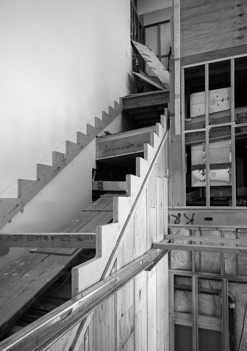 Black and white photo of CNR Group custom millwork showing an in-progress wooden staircase structure under construction inside a building.