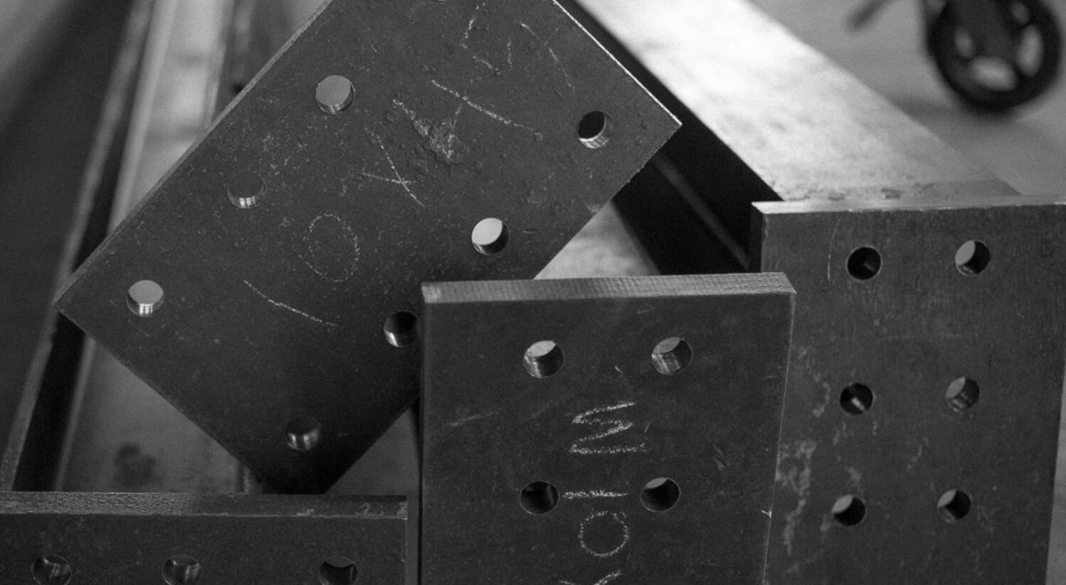 Close-up of several black metal plates with multiple drilled holes and chalk markings stacked on a flat surface, showcasing the work of NYC luxury home builders CNR Group.