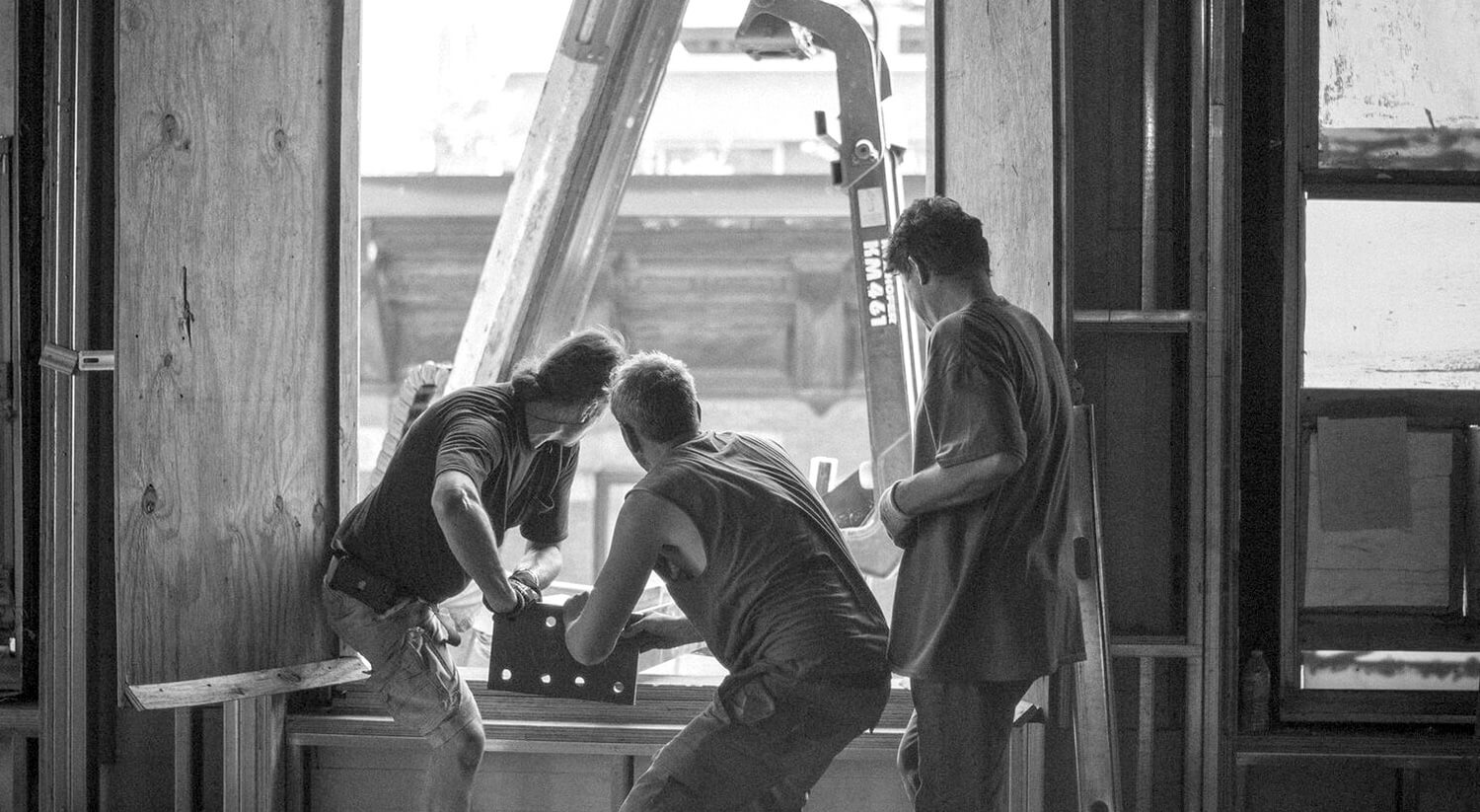 Three CNR Group NYC luxury home construction workers collaborating inside a building frame near a large window opening with a forklift arm outside.