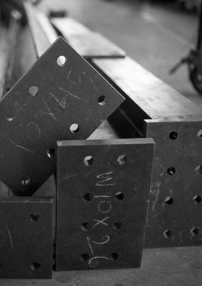 Close-up of metal plates with multiple holes stacked together, some with chalk markings from the work of CNR Group luxury home construction.