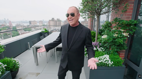 Man wearing sunglasses and a black suit standing on a rooftop terrace of a CNR Group NYC luxury home build with green plants and city buildings in the background.