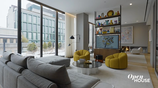 Modern living room of an NYC luxury home built by CNR Group with large floor-to-ceiling windows, gray sectional sofa, yellow armchairs, glass coffee table, and decorative shelving.