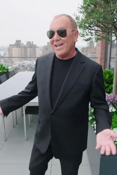 Man wearing black suit and sunglasses standing on a rooftop terrace of a CNR Group NYC luxury home with city buildings and greenery in the background.