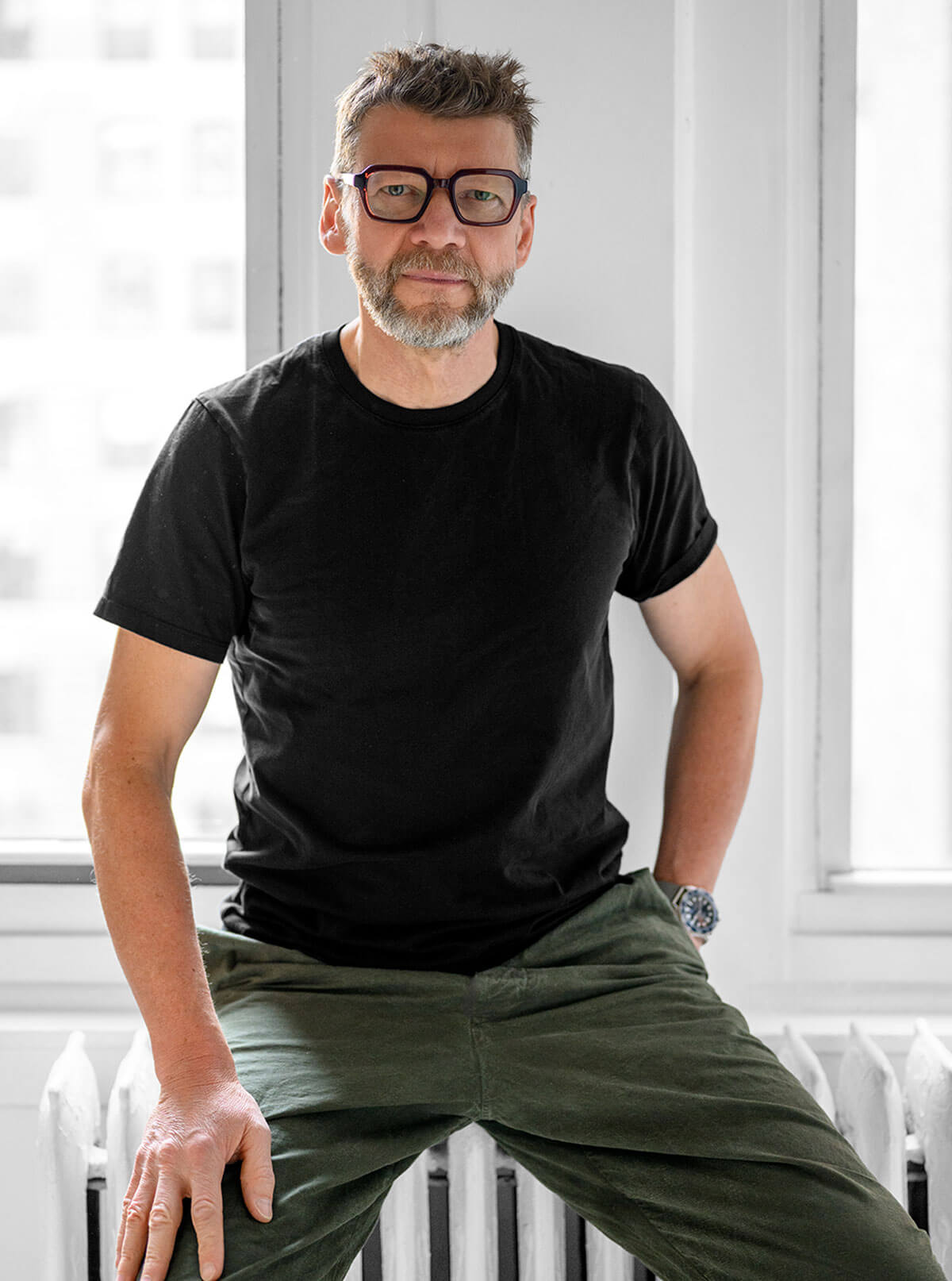 Jesse sitting on a stool looking at the camera. Black t-shirt and green pants.