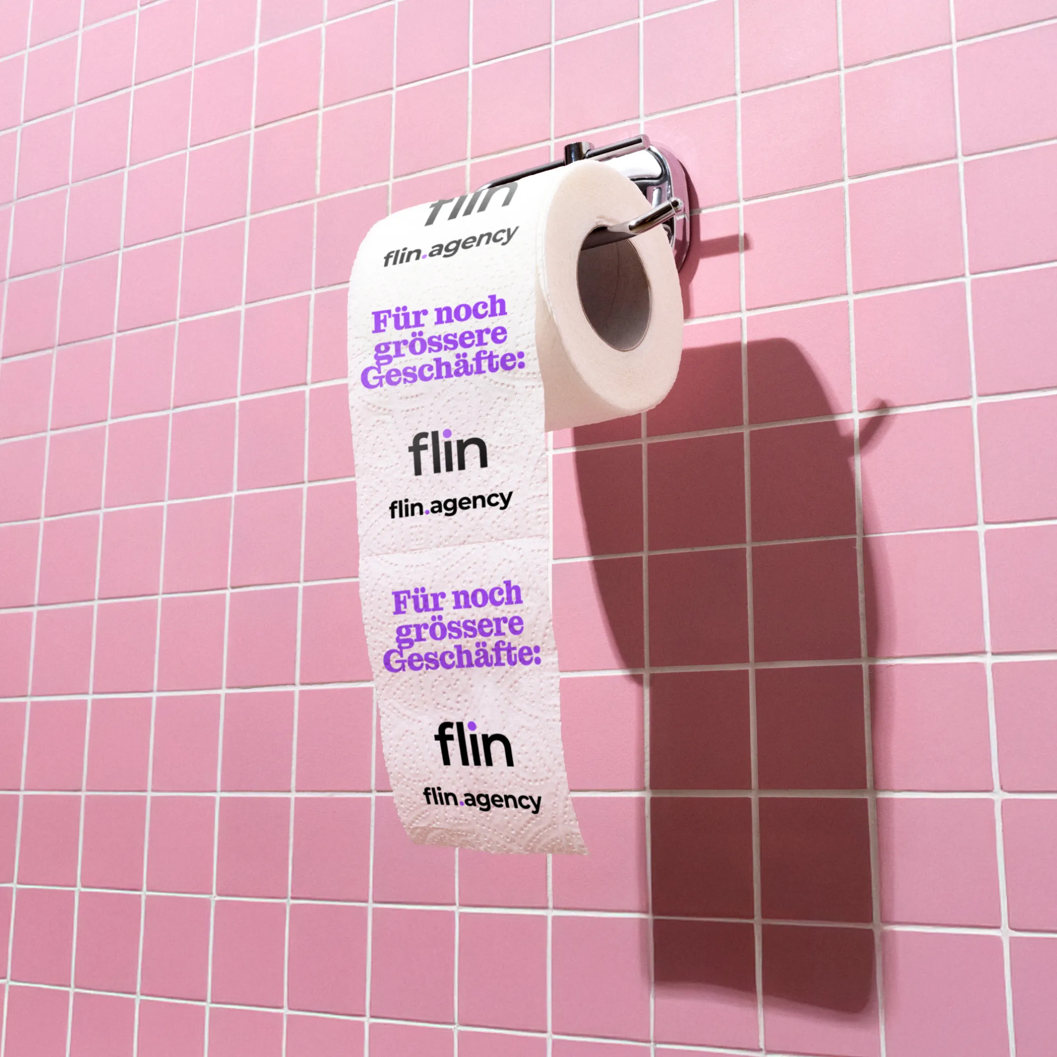 Rolle WC-Papier an einer rosa gefliesten Wand, bedruckt mit Flin-Logo und violettem Schriftzug ‚Für noch grössere Geschäfte:‘.