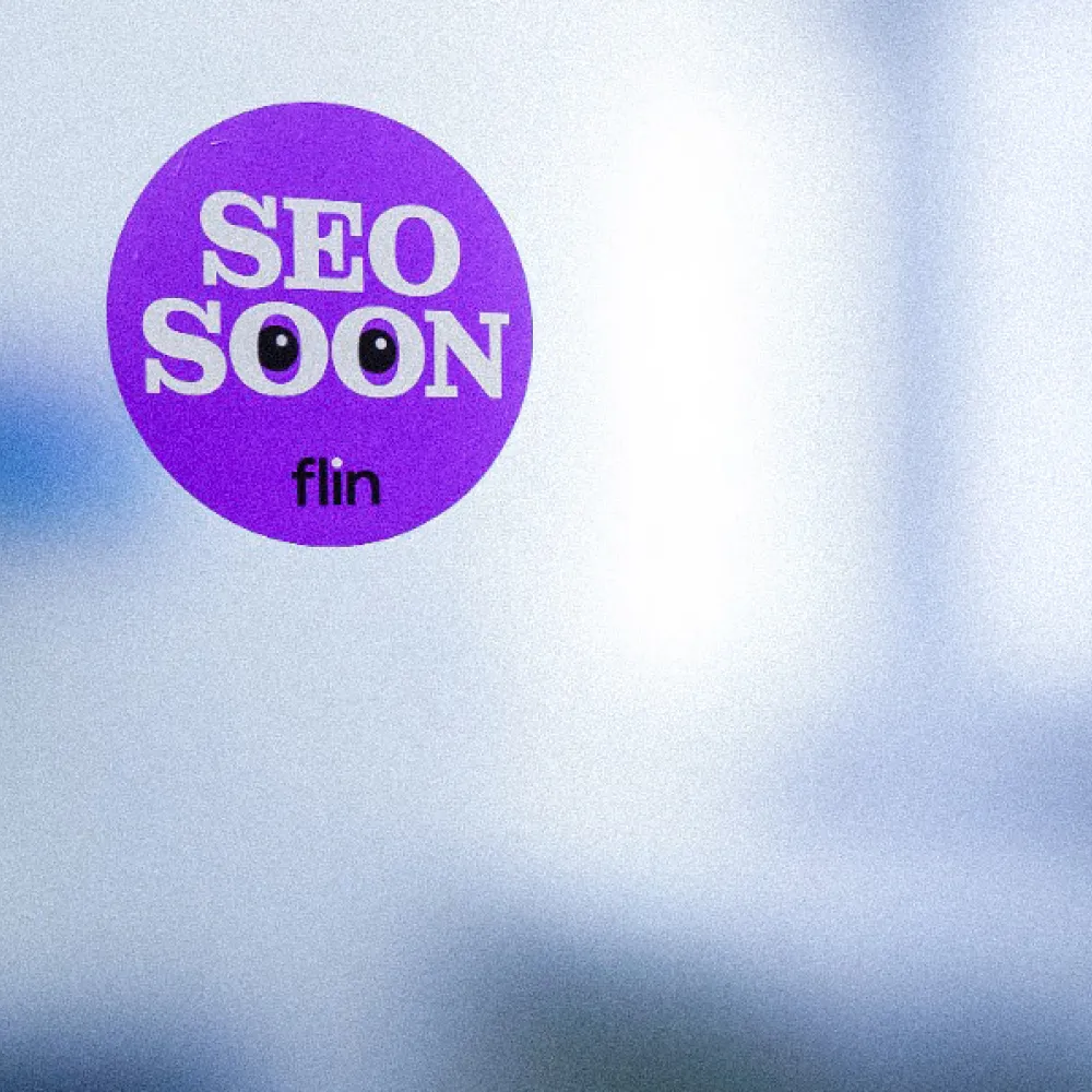 under violetter Sticker mit weisser Aufschrift ‚SEO SOON‘ und zwei Augen in den Buchstaben O, darunter Flin-Logo, an einer Glasscheibe angebracht.