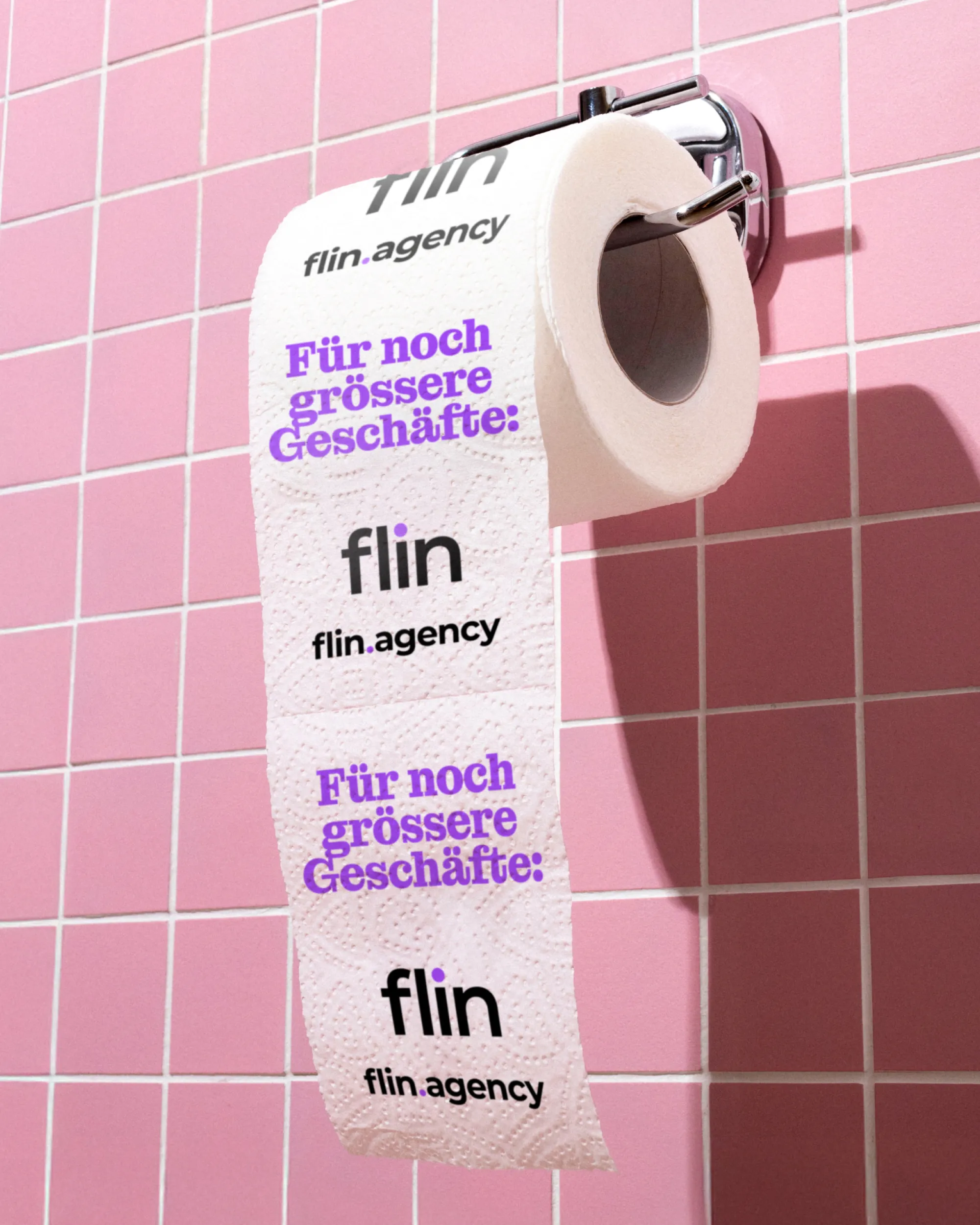 Rolle WC-Papier an einer rosa gefliesten Wand, bedruckt mit Flin-Logo und violettem Schriftzug ‚Für noch grössere Geschäfte:‘.