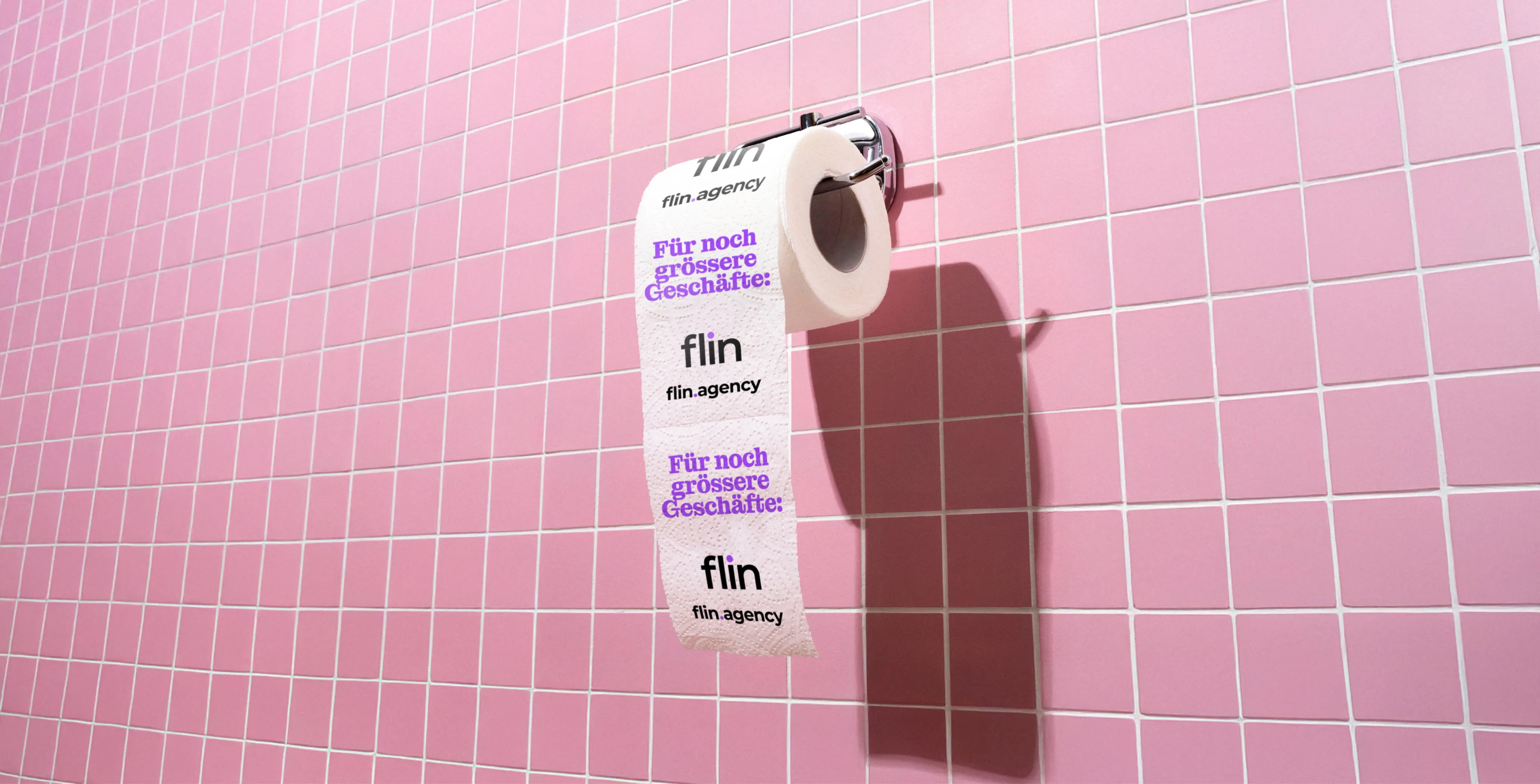 Rolle WC-Papier an einer rosa gefliesten Wand, bedruckt mit Flin-Logo und violettem Schriftzug ‚Für noch grössere Geschäfte:‘.