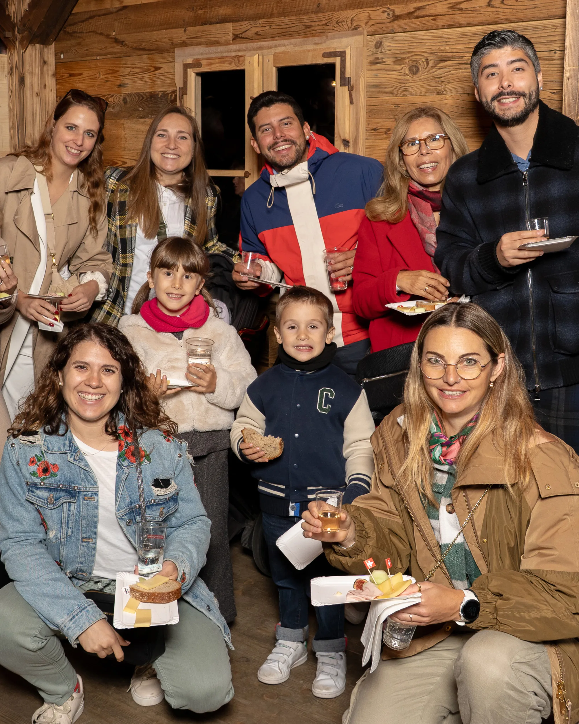 Erwachsene und Kinder beim Tilsiter-Publikumsaktien-Apéro in einer Holzhütte mit Getränken und Snacks.