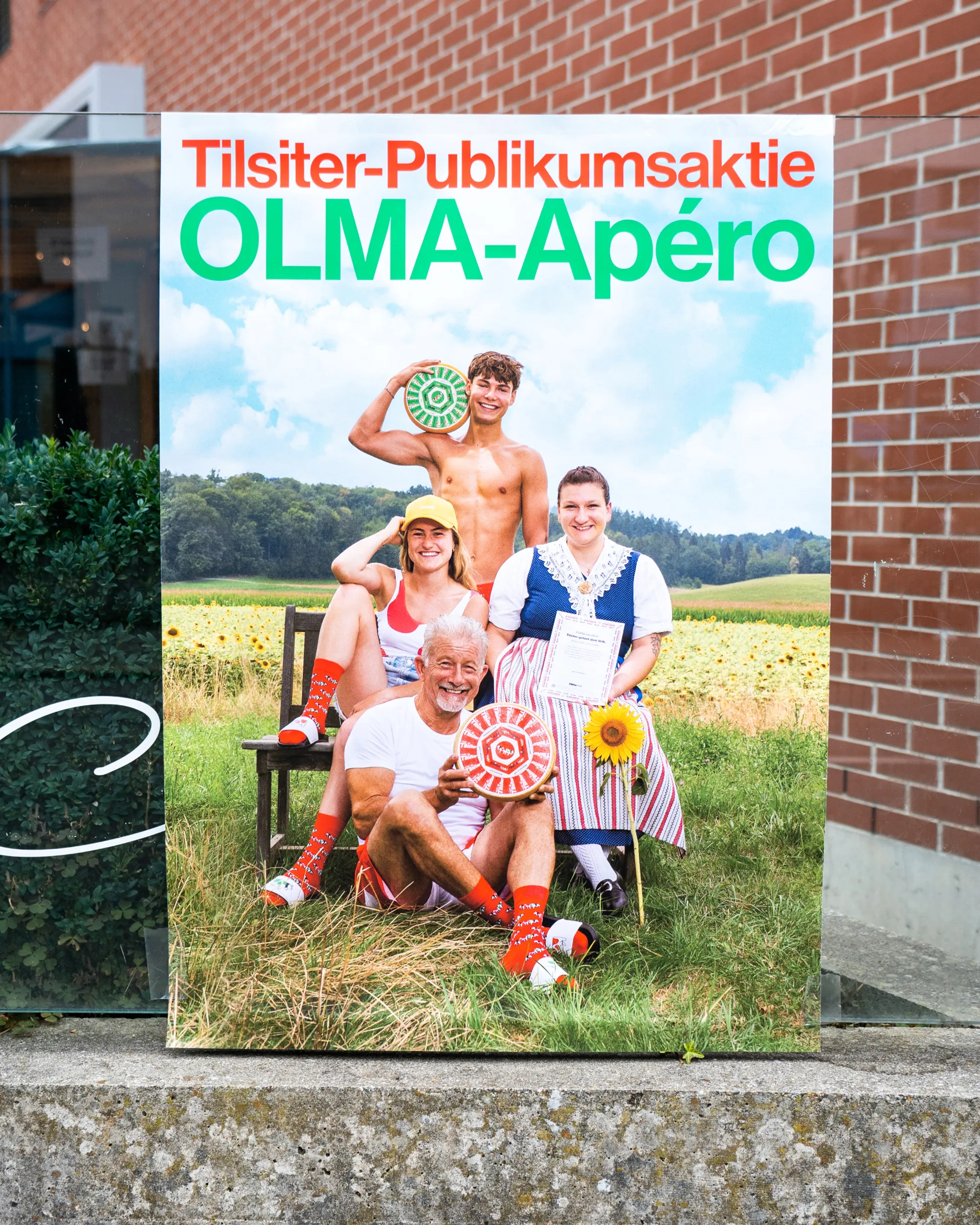 Werbeplakat zum Tilsiter-Publikumsaktien-Apéro mit mehreren Personen in einer ländlichen Szene.