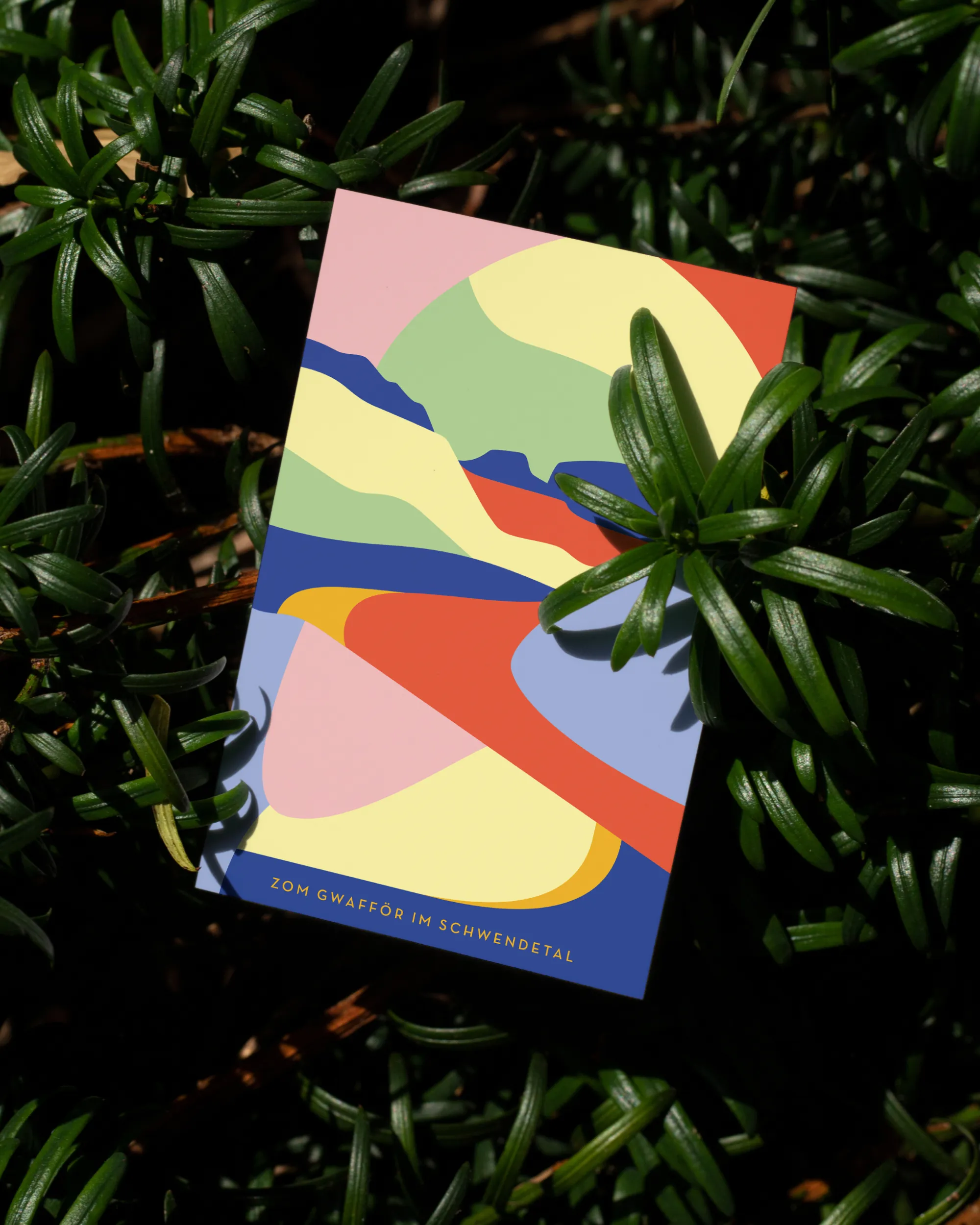 Bunte Visitenkarte von Zom Gwafför mit abstrakter Landschaftsillustration, arrangiert zwischen grünen Blättern.