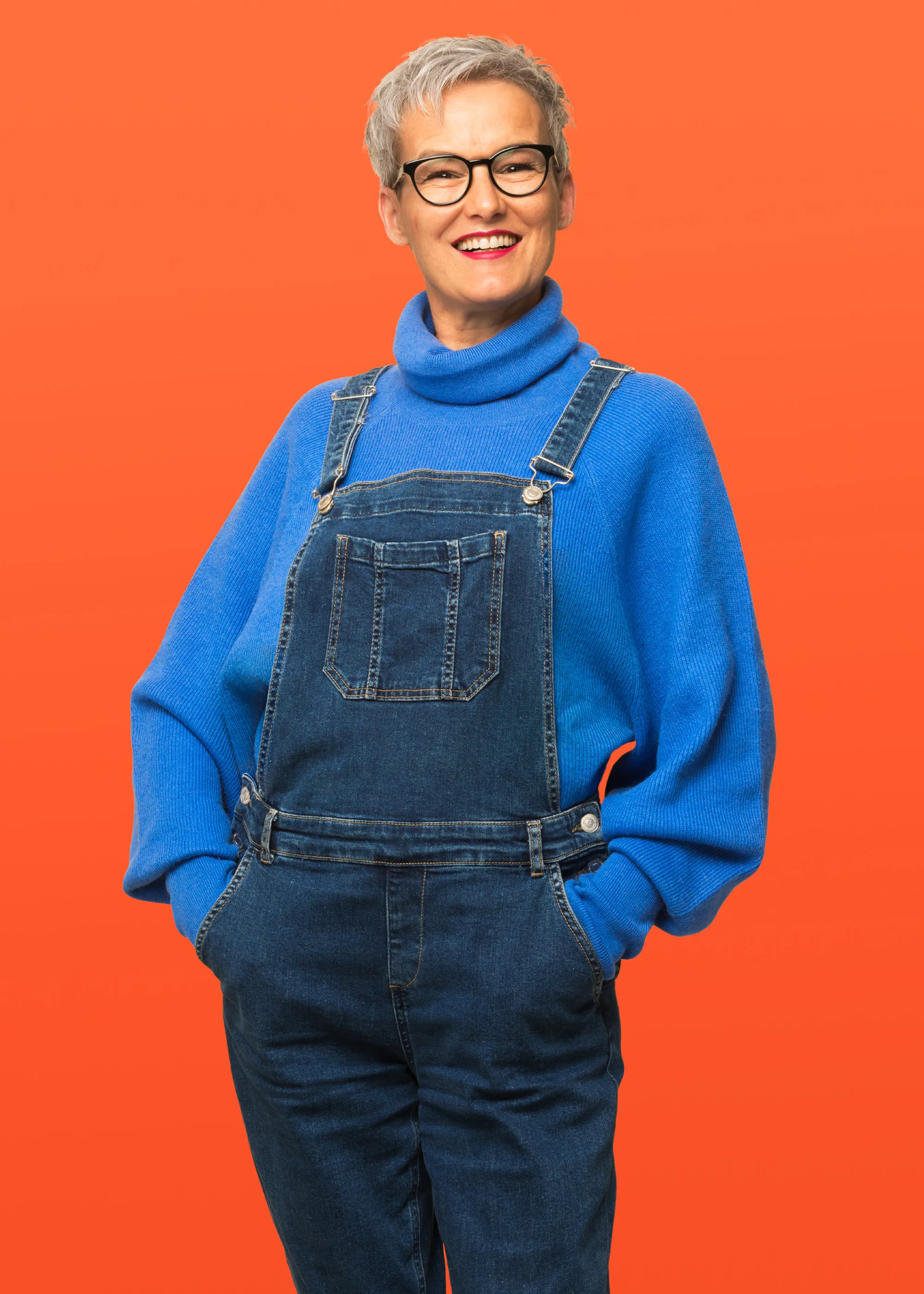 Frau mit Brille und blauer Kleidung vor orangem Hintergrund – selbstbewusstes Porträt von Zom Gwafför.