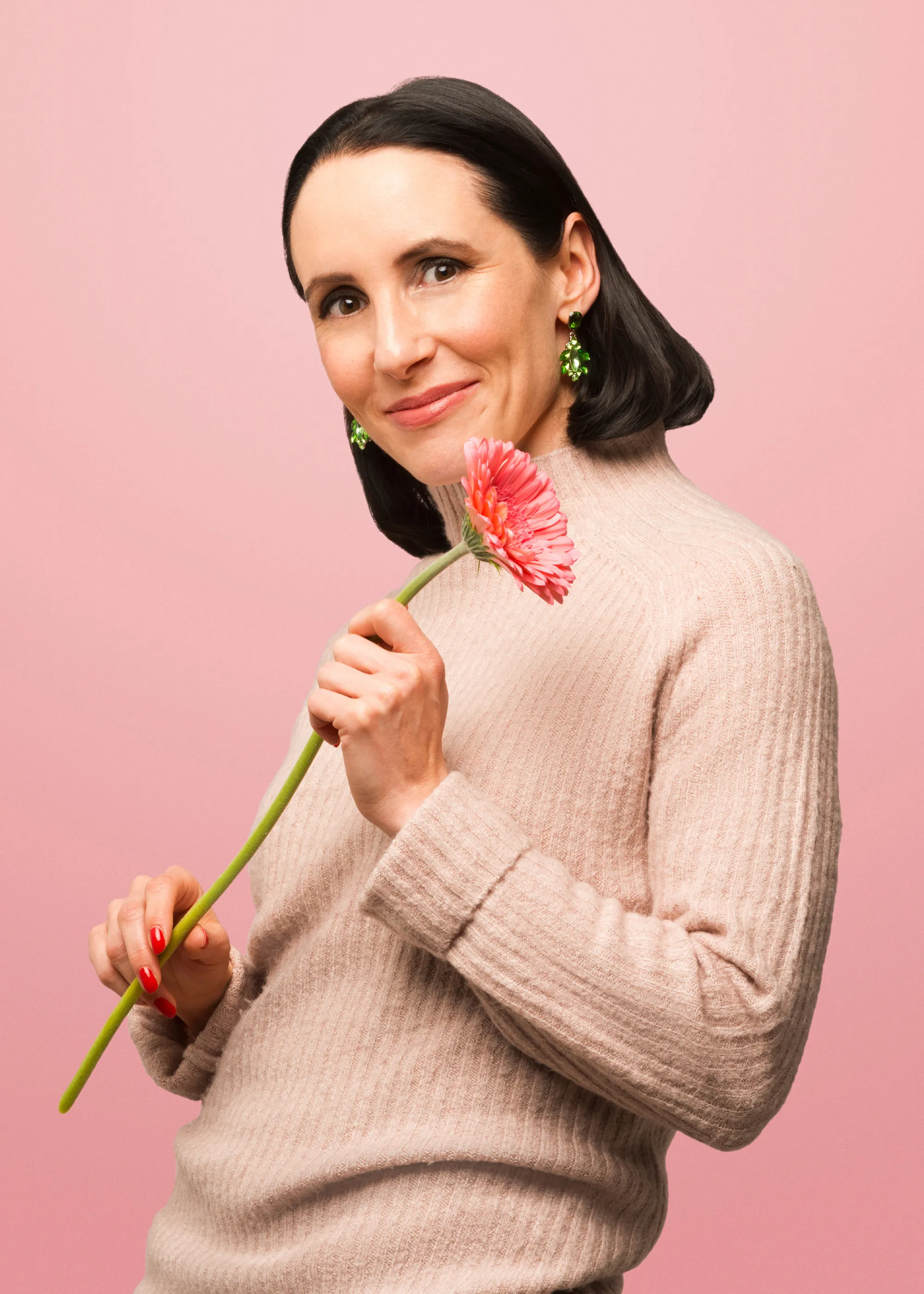 Frau mit dunklem Haar und pinker Blume in der Hand vor roséfarbenem Hintergrund – Zom Gwafför Kampagnenmotiv.