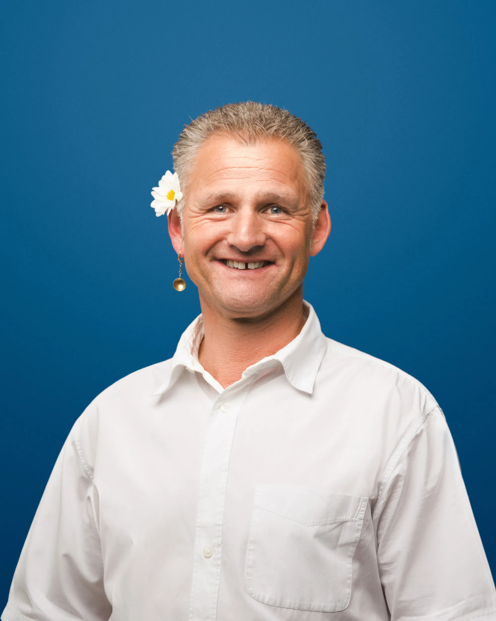 Lächelnder Mann mit Blume im Haar vor blauem Hintergrund, Kampagnenmotiv von Zom Gwafför.