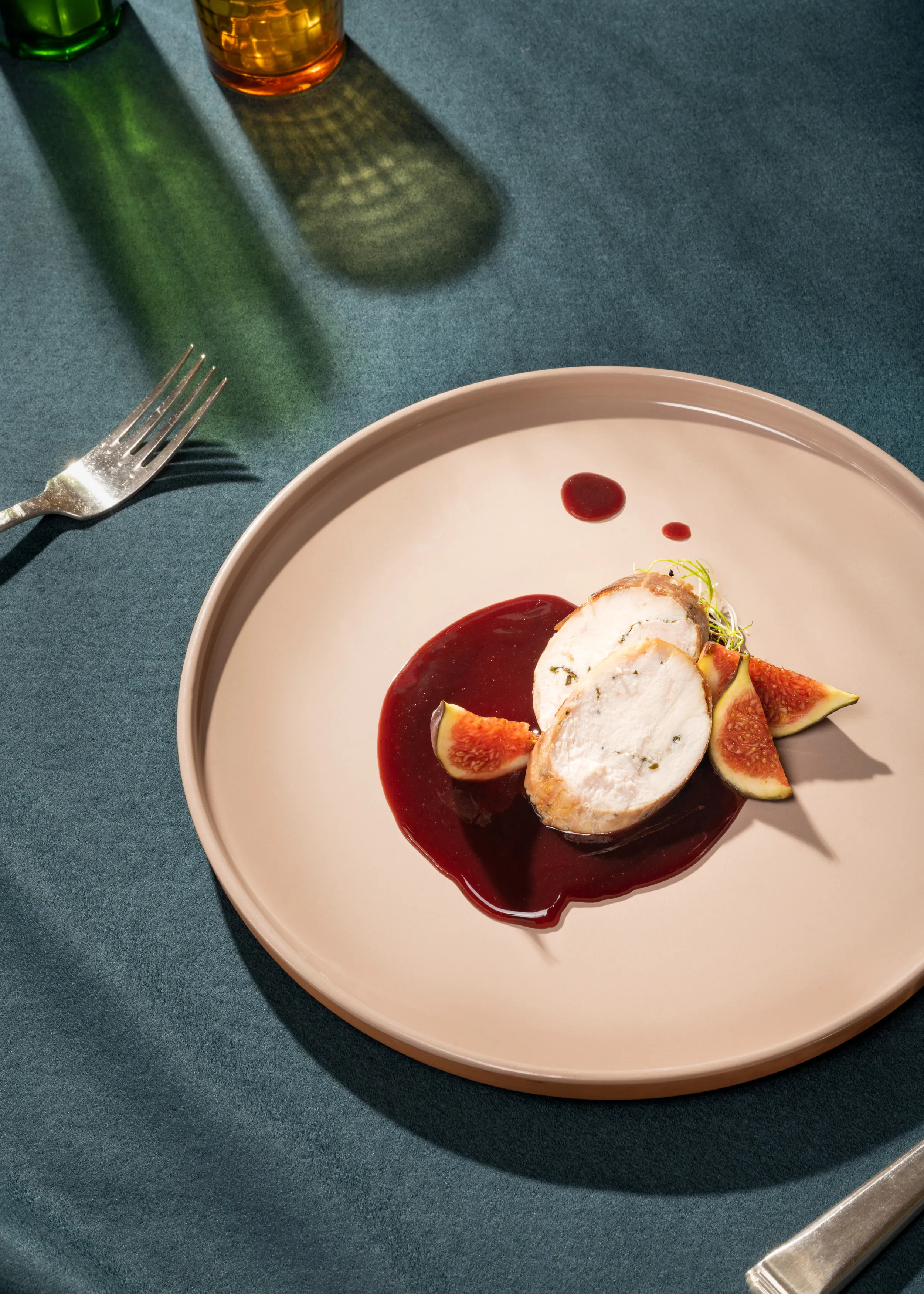 Aufgeschnittene Poulet-Roulade auf hellem Teller, angerichtet in dunkler Feigensauce mit frischen Feigenspalten, fotografiert auf blauer Tischfläche mit Glasreflexionen im Hintergrund.