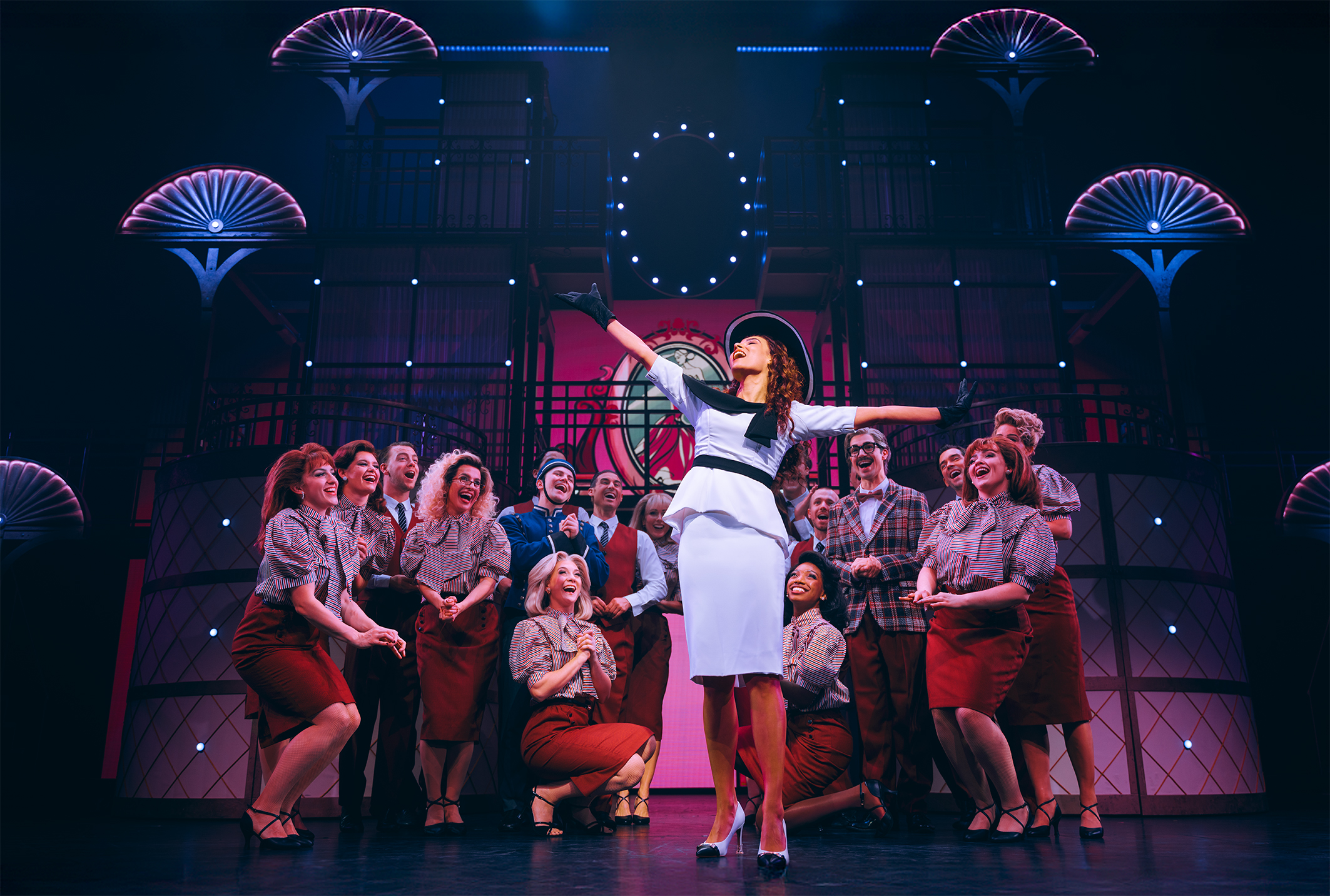 Vivian im weißen Kleid beim Shopping, Ensemble als Verkäufer*innen im Hintergrund