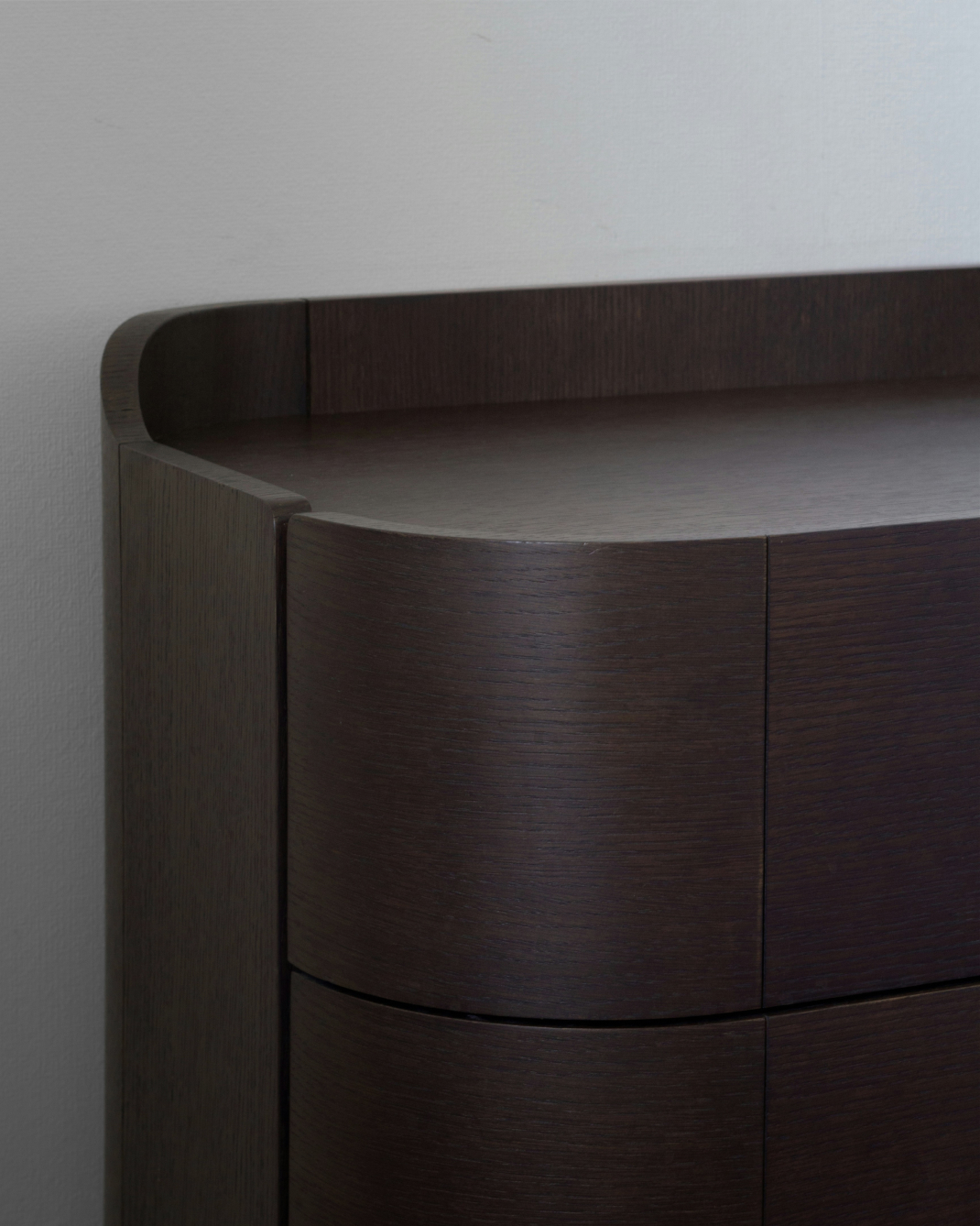 A photo of a curved dark wood dresser with natural grains.