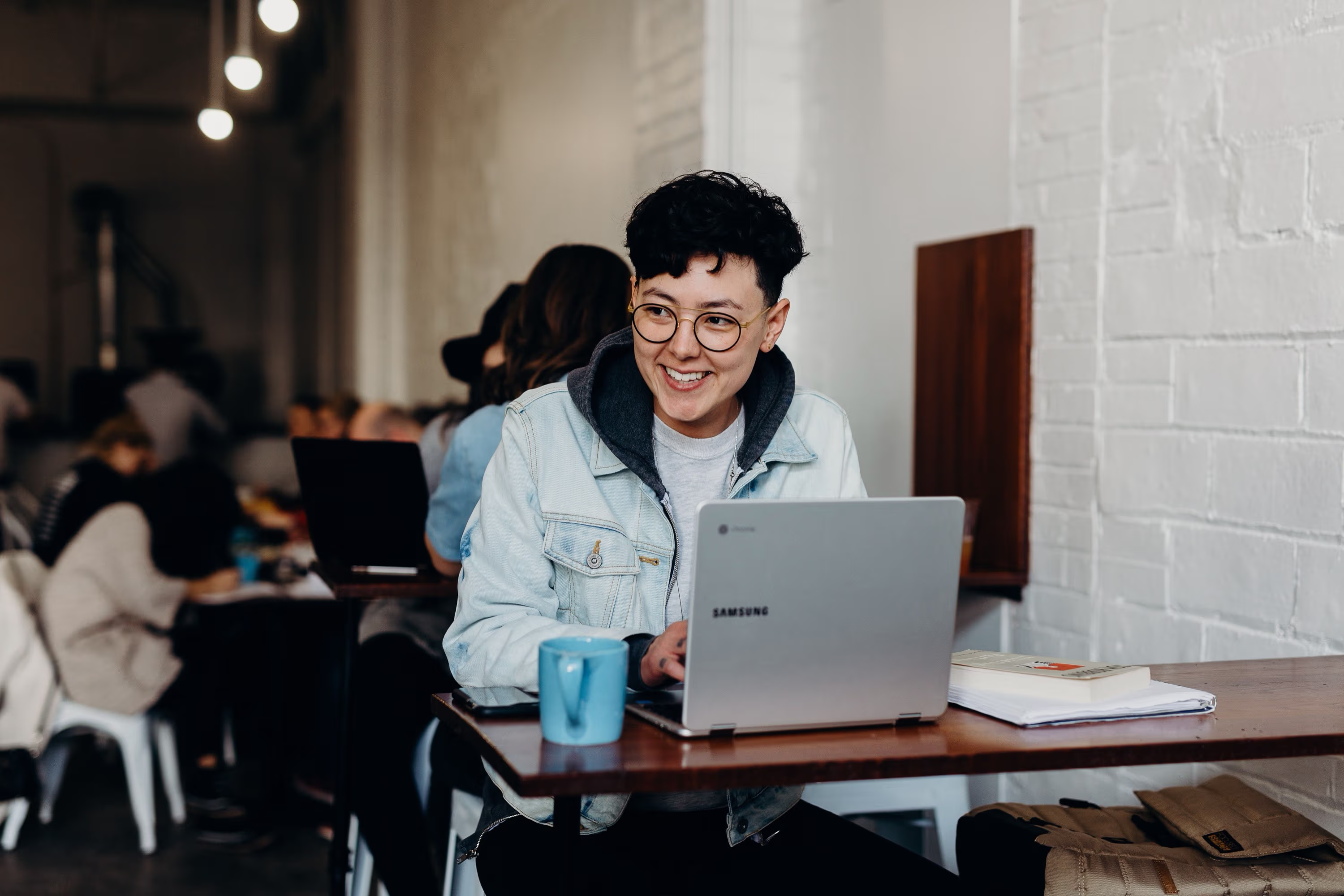 Person sitzt am Laptop mit Kaffee in einem belebten Cafe