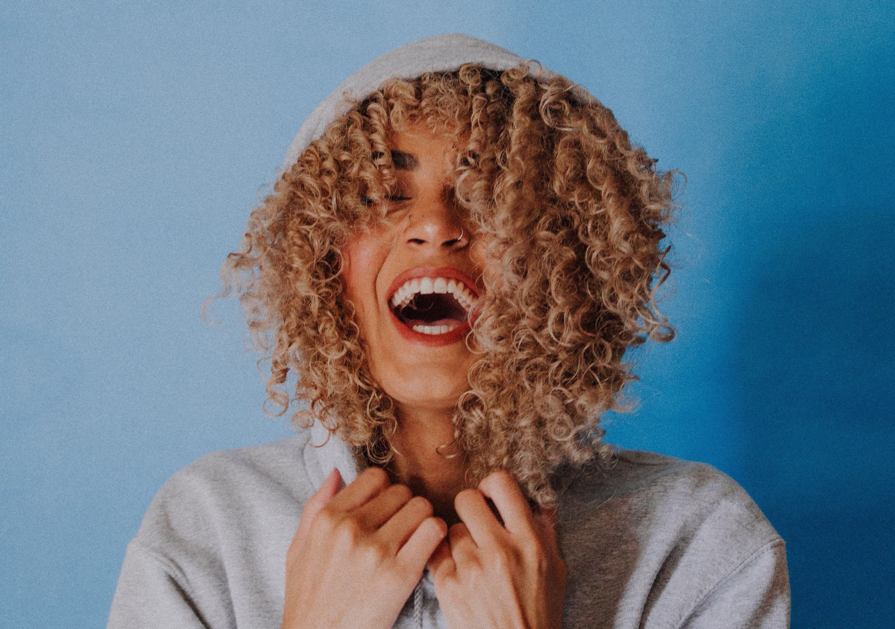 Woman laughing and pulling a hood over her curly hair